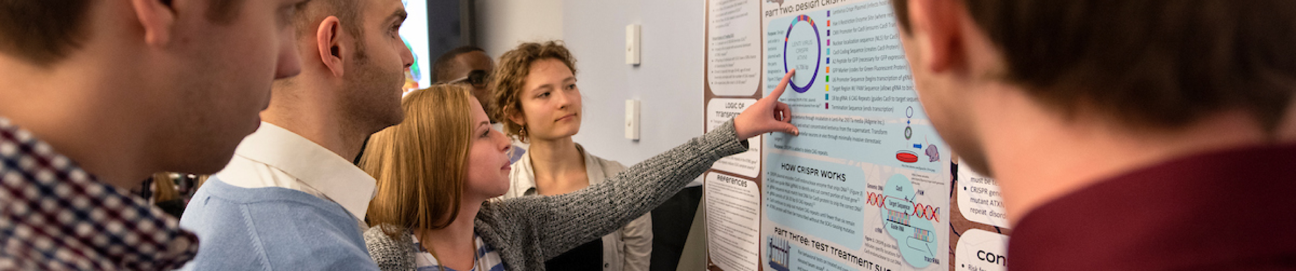 student pointing at research poster with group of students listening